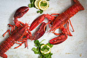 Two lobsters on a cutting board with lemons and parsley